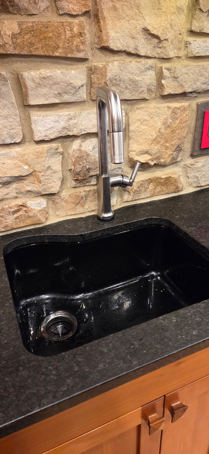 Black granite kitchen sink with chrome faucet against a stone tile backsplash.