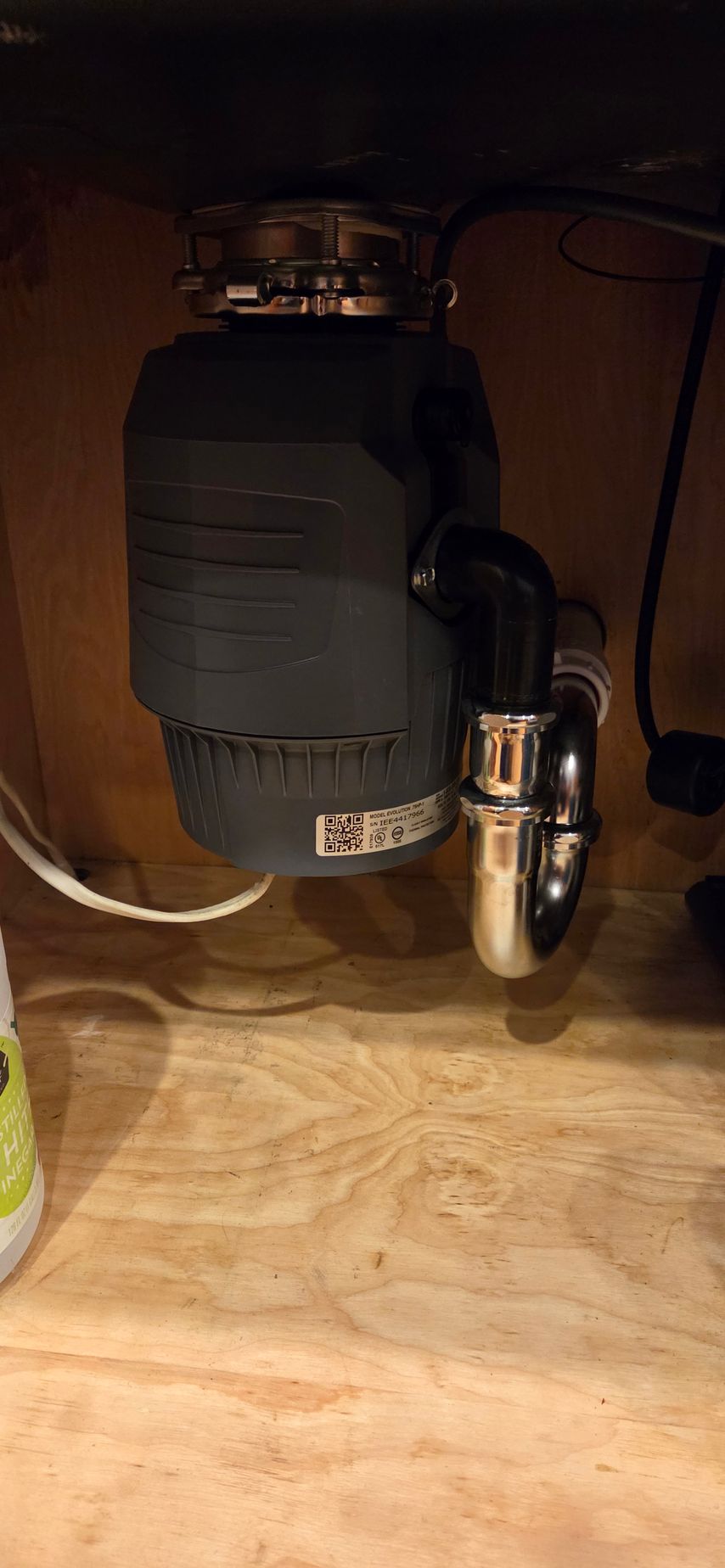 Black coffee maker under a kitchen cabinet on a wooden countertop, with a metal kettle beside it.