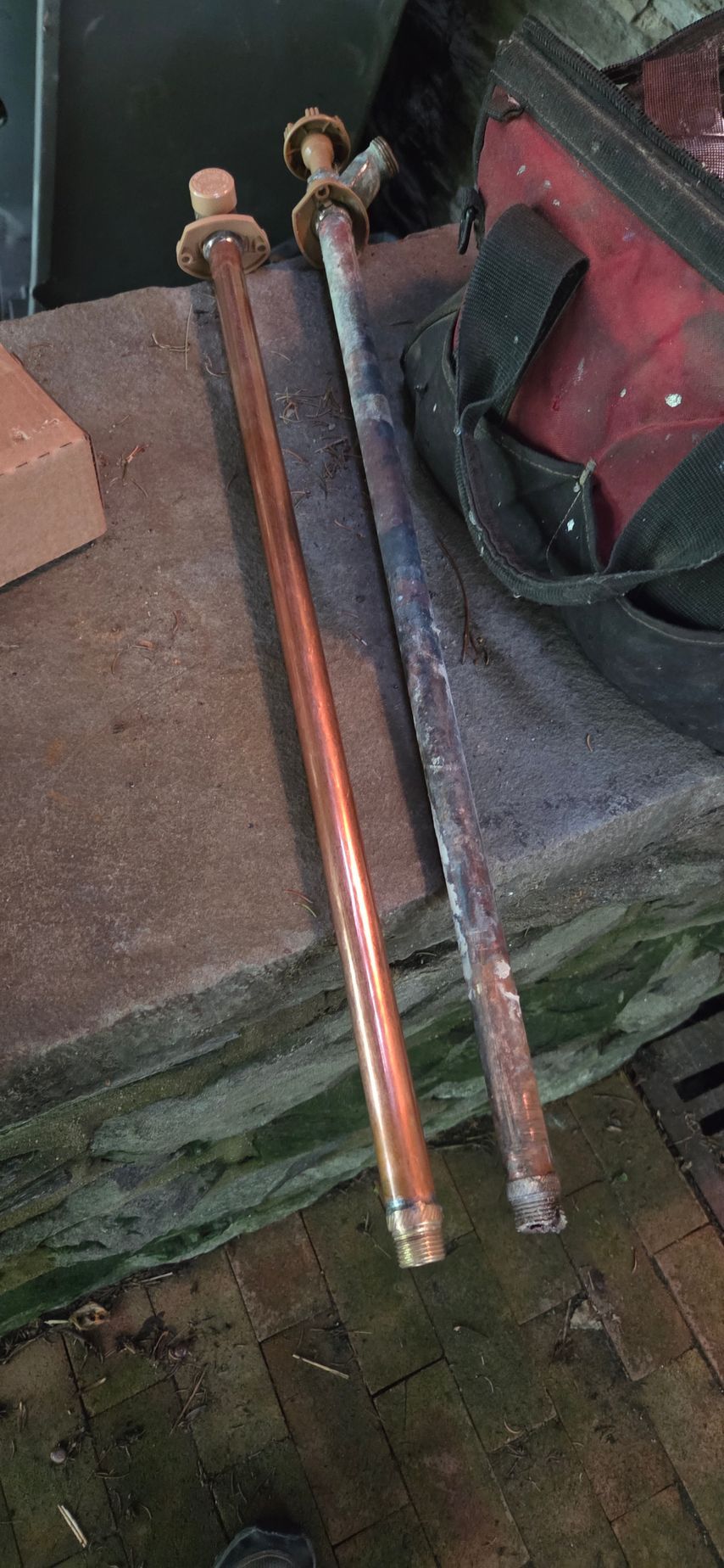 Two copper-colored metal rods with bolts leaning against a worn green bench and a red bag.