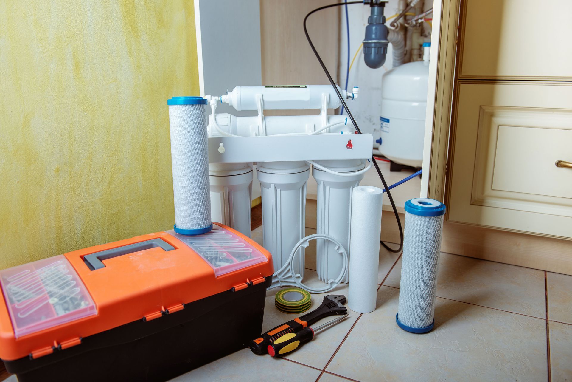 Water filter system with white cartridges, blue caps, and orange toolbox on a tiled floor