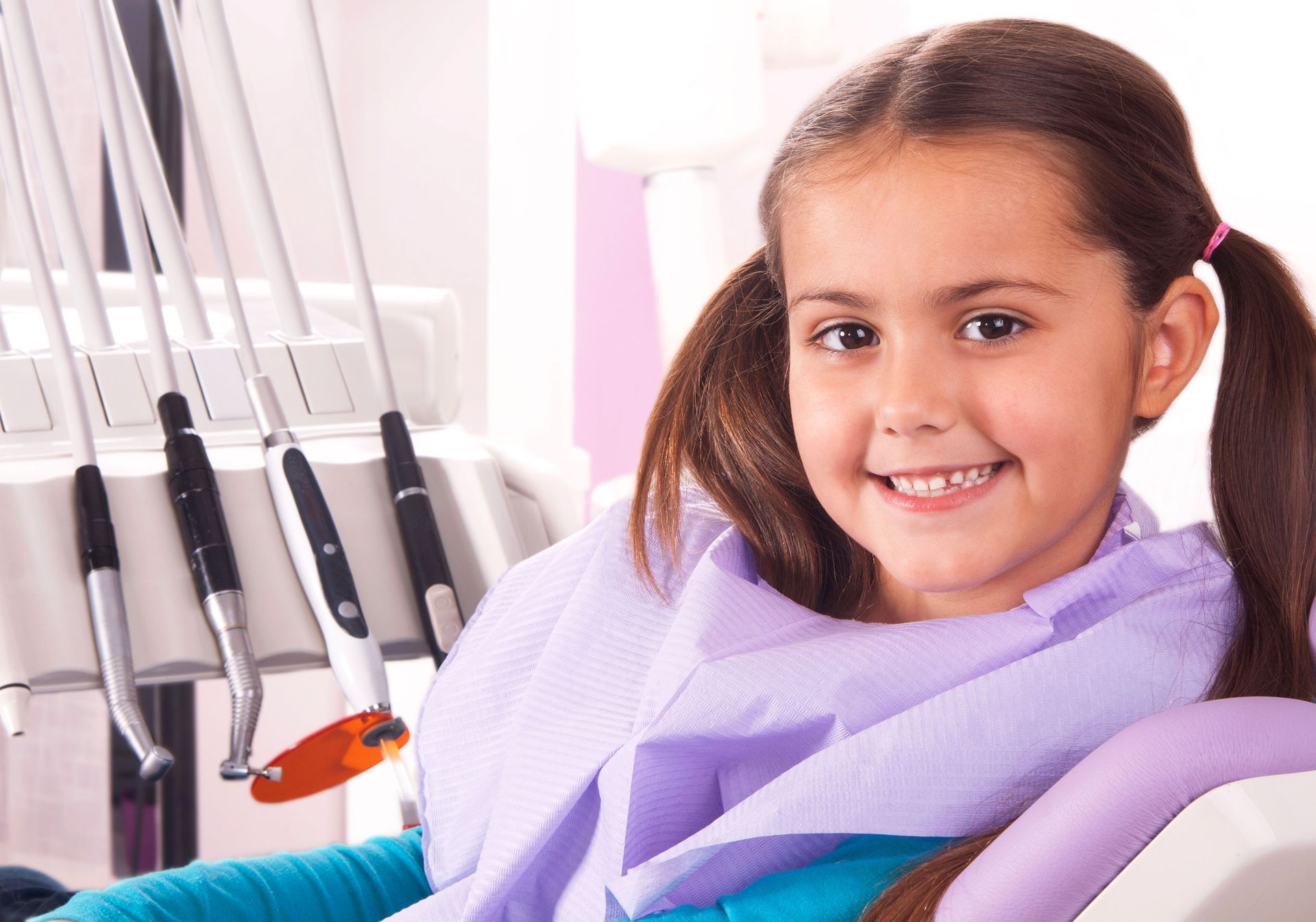 A little girl is sitting in a dental chair and smiling.