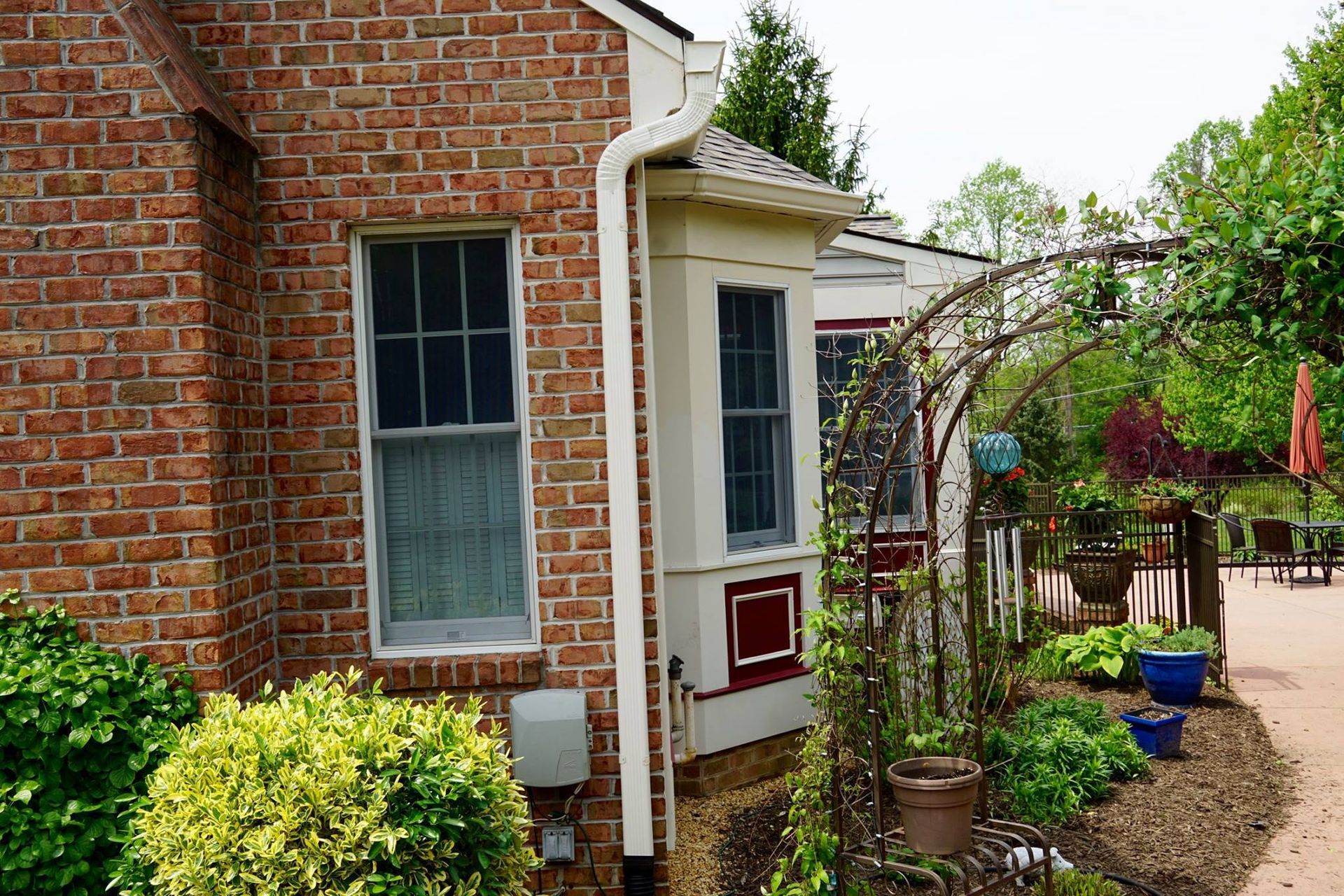 Red brick house with windows, white trim, and a garden with an archway.