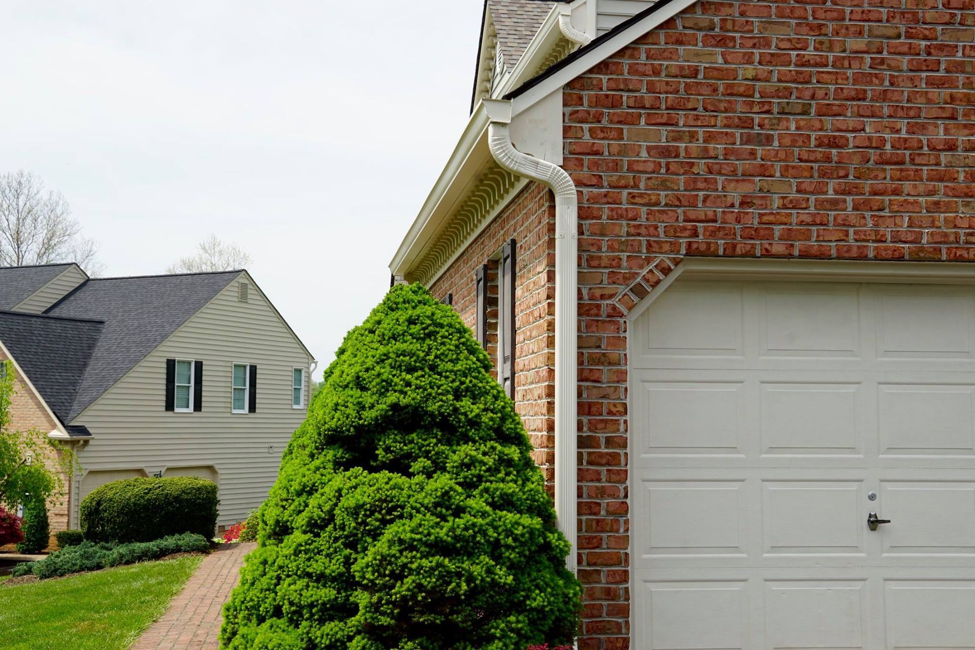 Brick house with white garage door, green shrub, and gray roof.