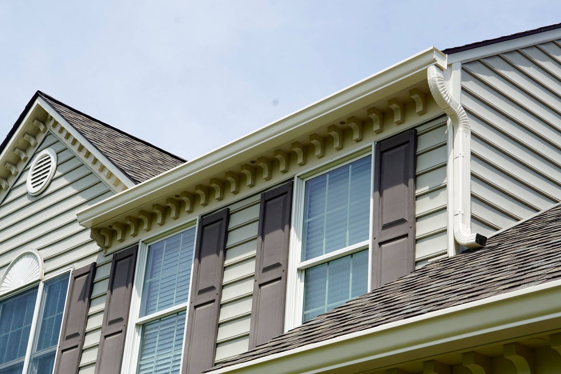 Beige house exterior with windows, brown shutters, and decorative trim.