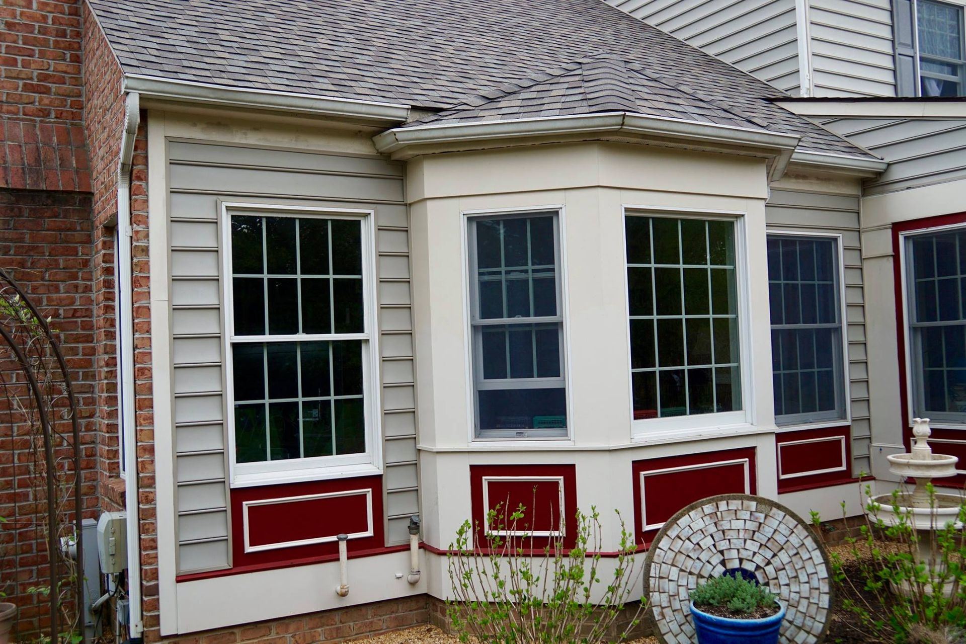 Exterior view of a house with gray siding, a bay window, and a brick chimney.