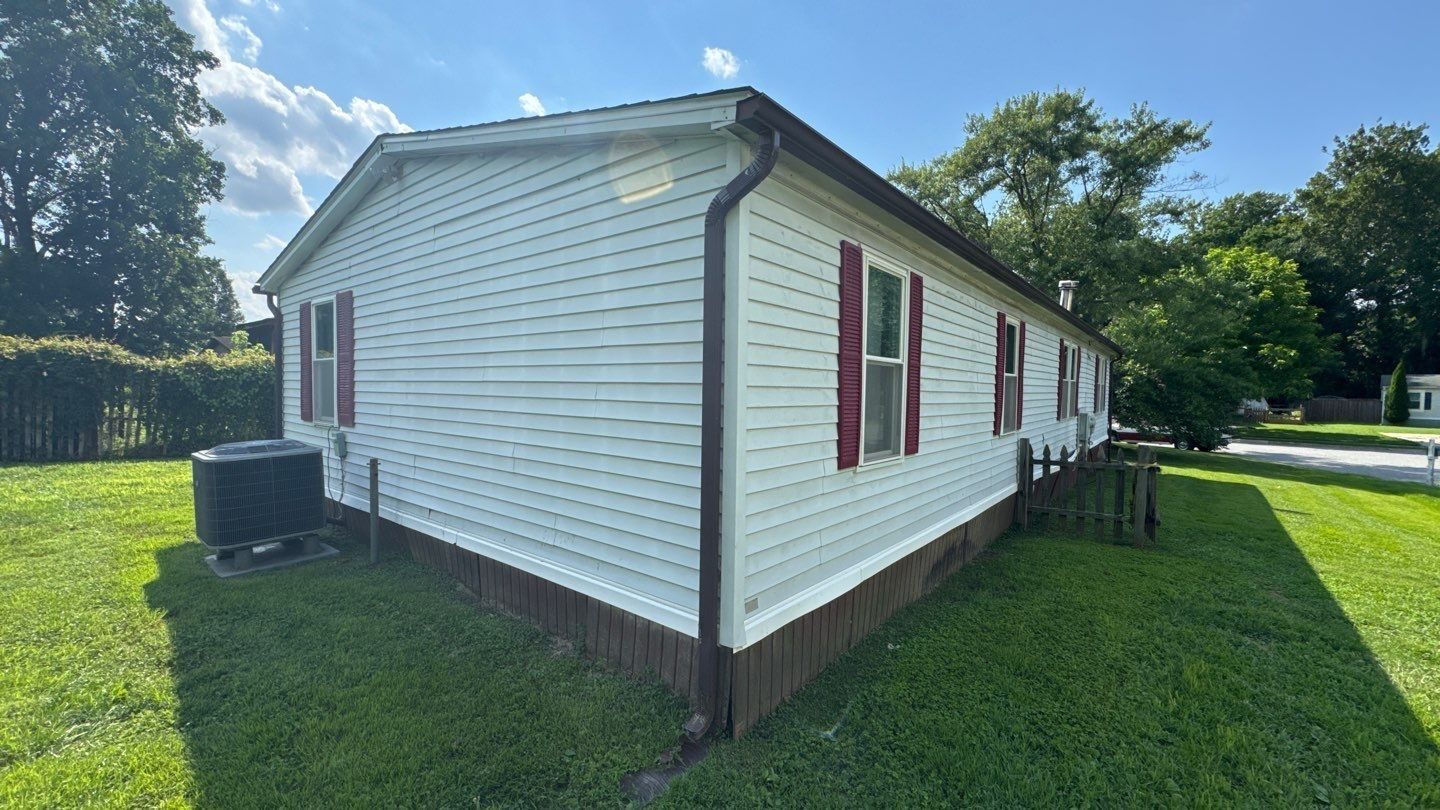 White-sided house with maroon shutters and brown trim on a grassy lawn under a partly cloudy sky.