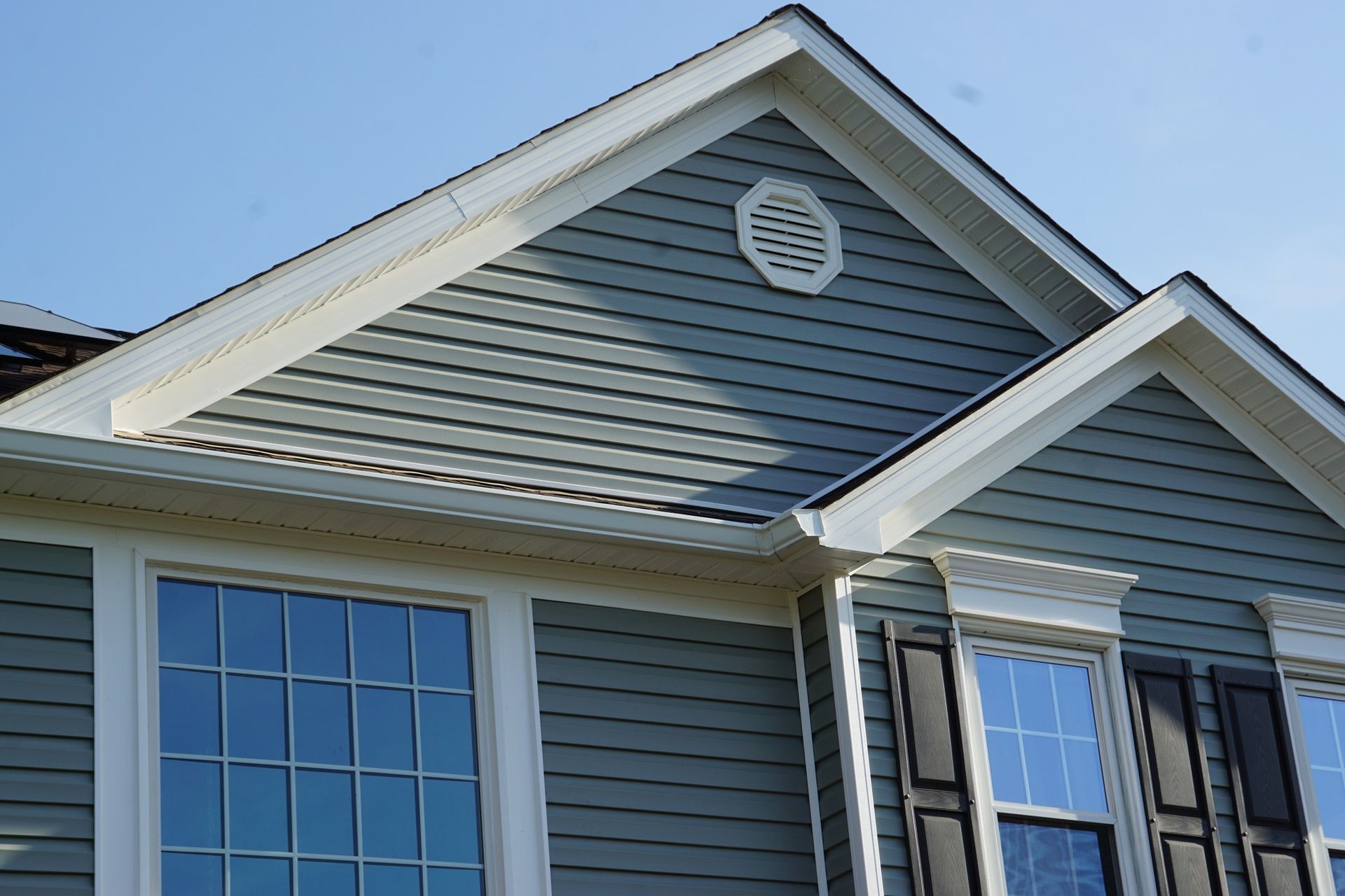 House exterior with blue siding, white trim, and black shutters under a clear sky.