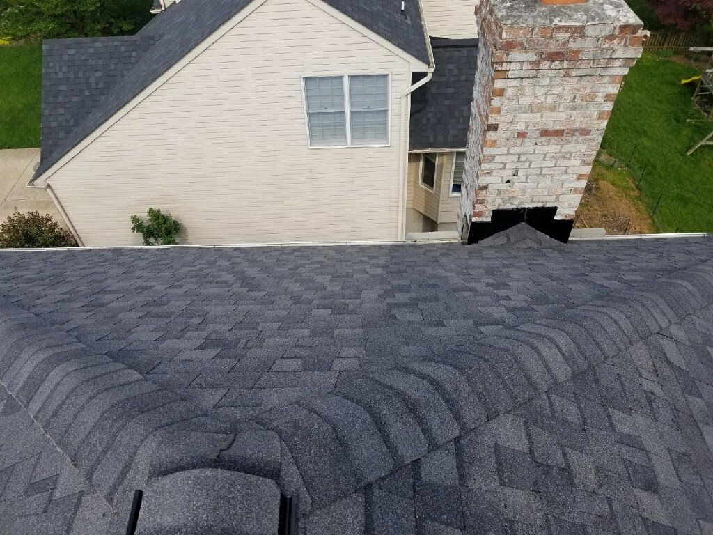 Dark gray shingled roof with a chimney and part of a light beige house. Green grass is visible.