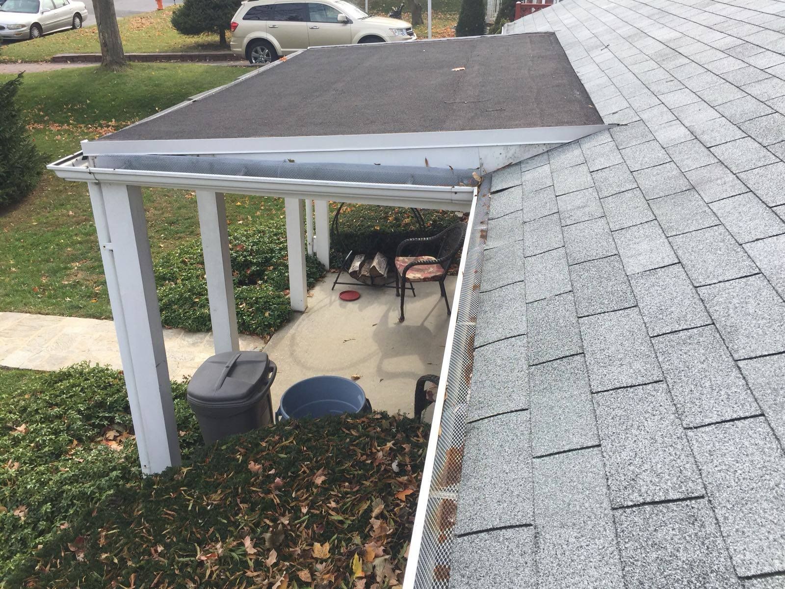 A gray shingled roof next to a covered patio with black roof, white support beams, and a trash can.