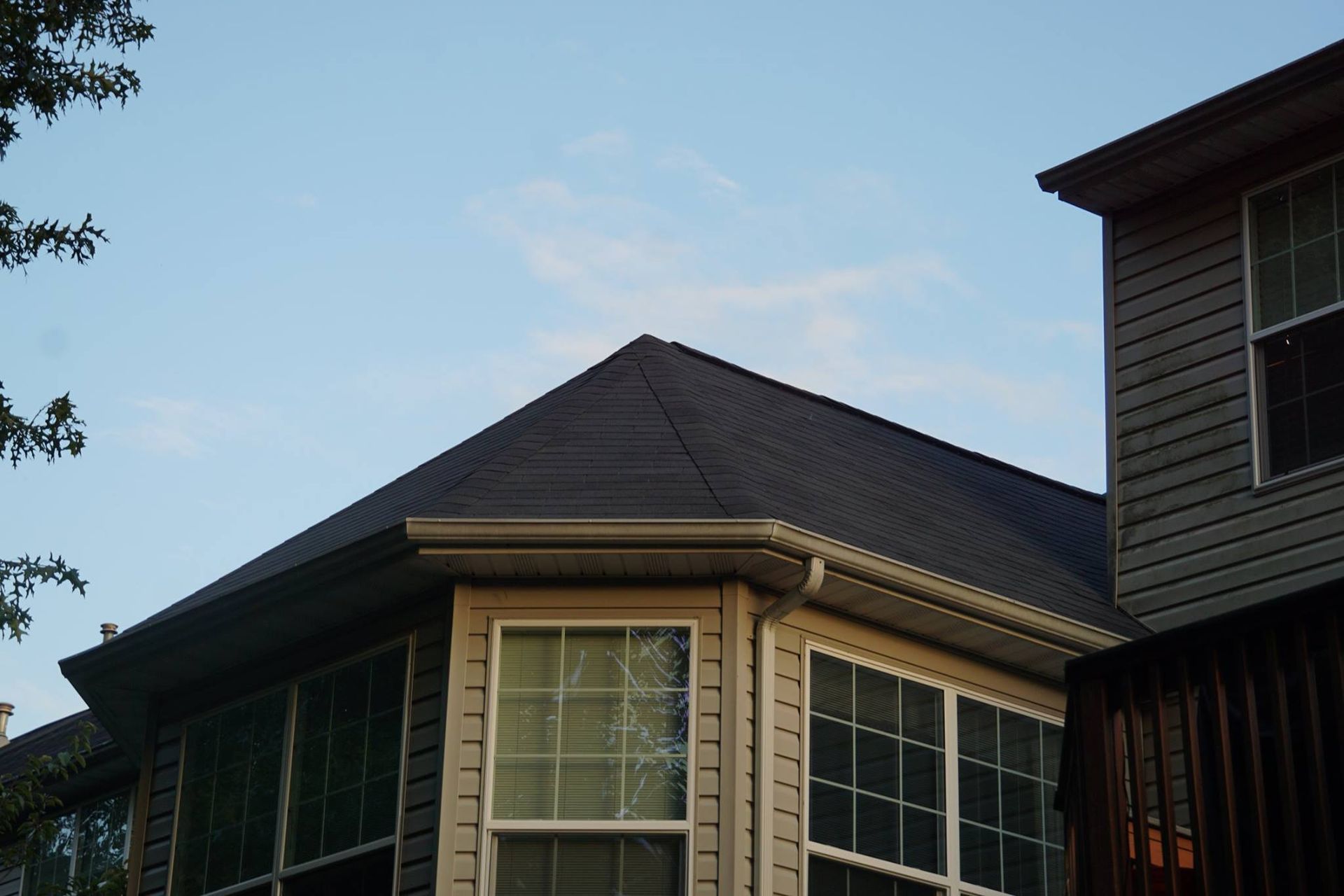 Dark gray roof of a house with white windows and siding against a blue sky.