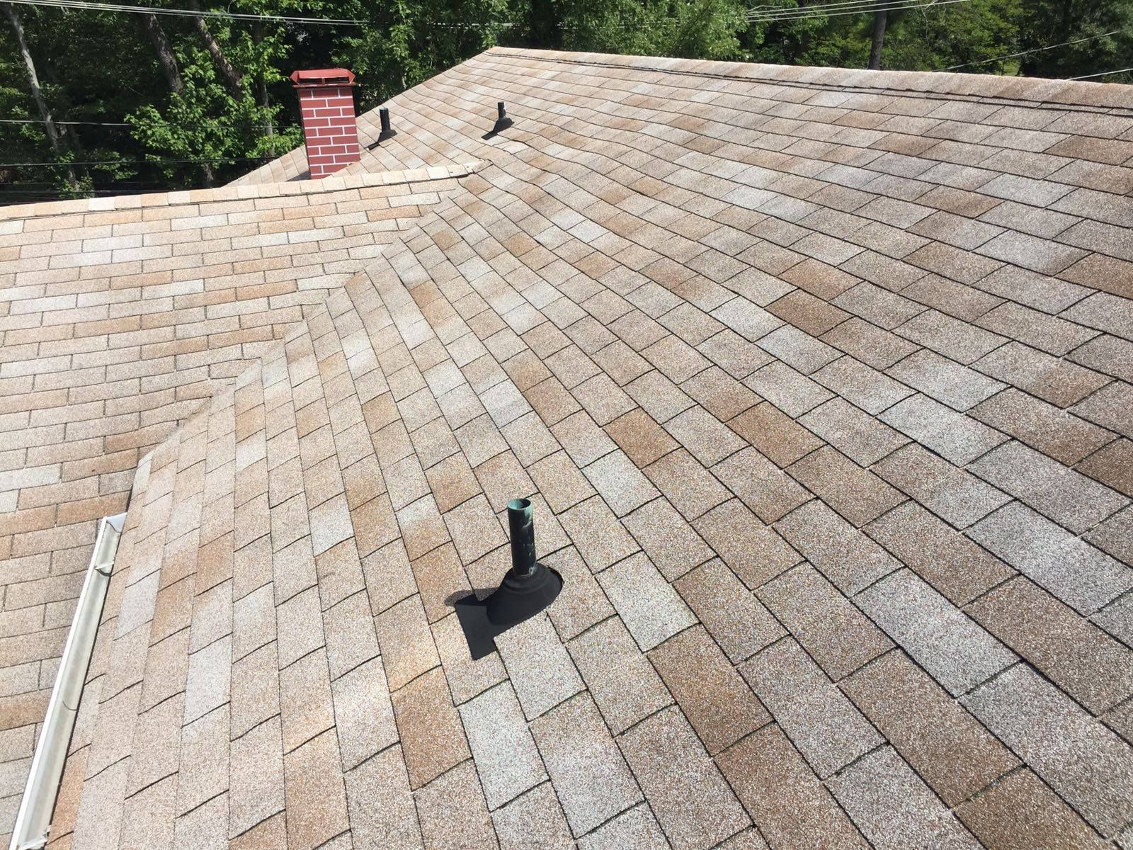 Brown and tan asphalt shingle roof with a red brick chimney and vent pipes.