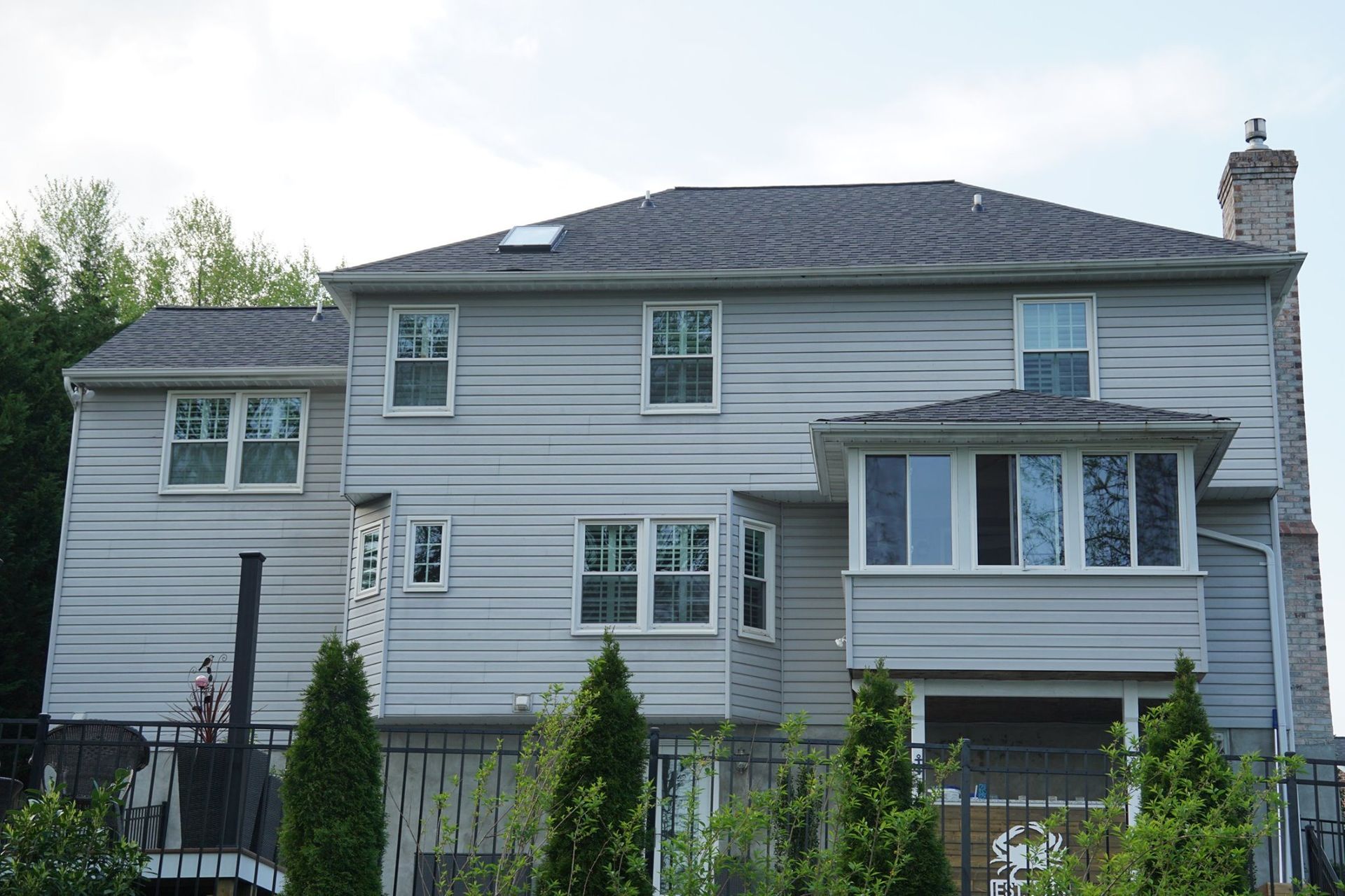 Gray-sided two-story house with multiple windows, a chimney, and a small roofed porch area. Trees in the foreground.