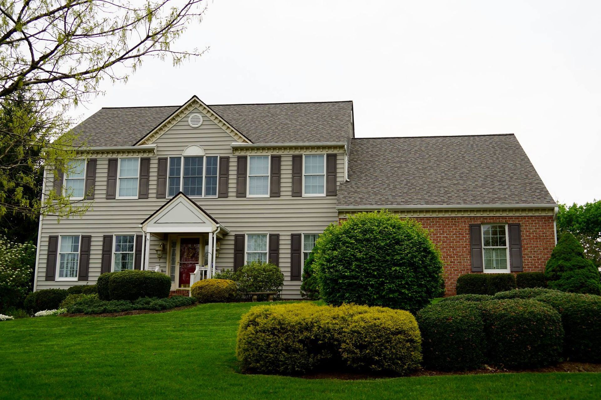 Two-story house with green lawn, shrubs, shutters, and brick exterior.
