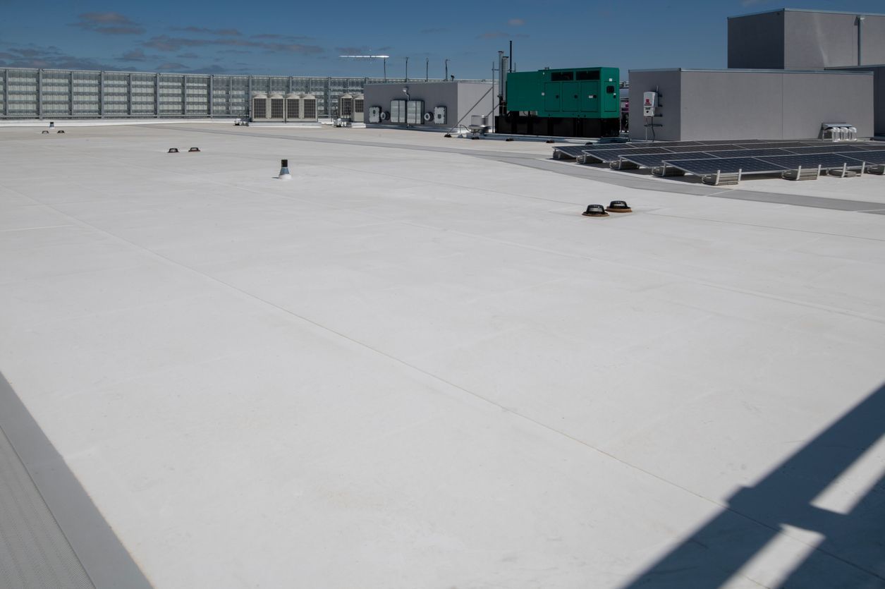 White flat roof with equipment and a partial view of a building with blue sky background.
