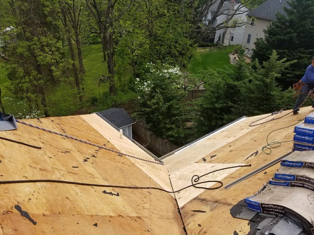 Roofing work in progress on a multi-angled roof with fresh plywood, a worker, and materials visible.