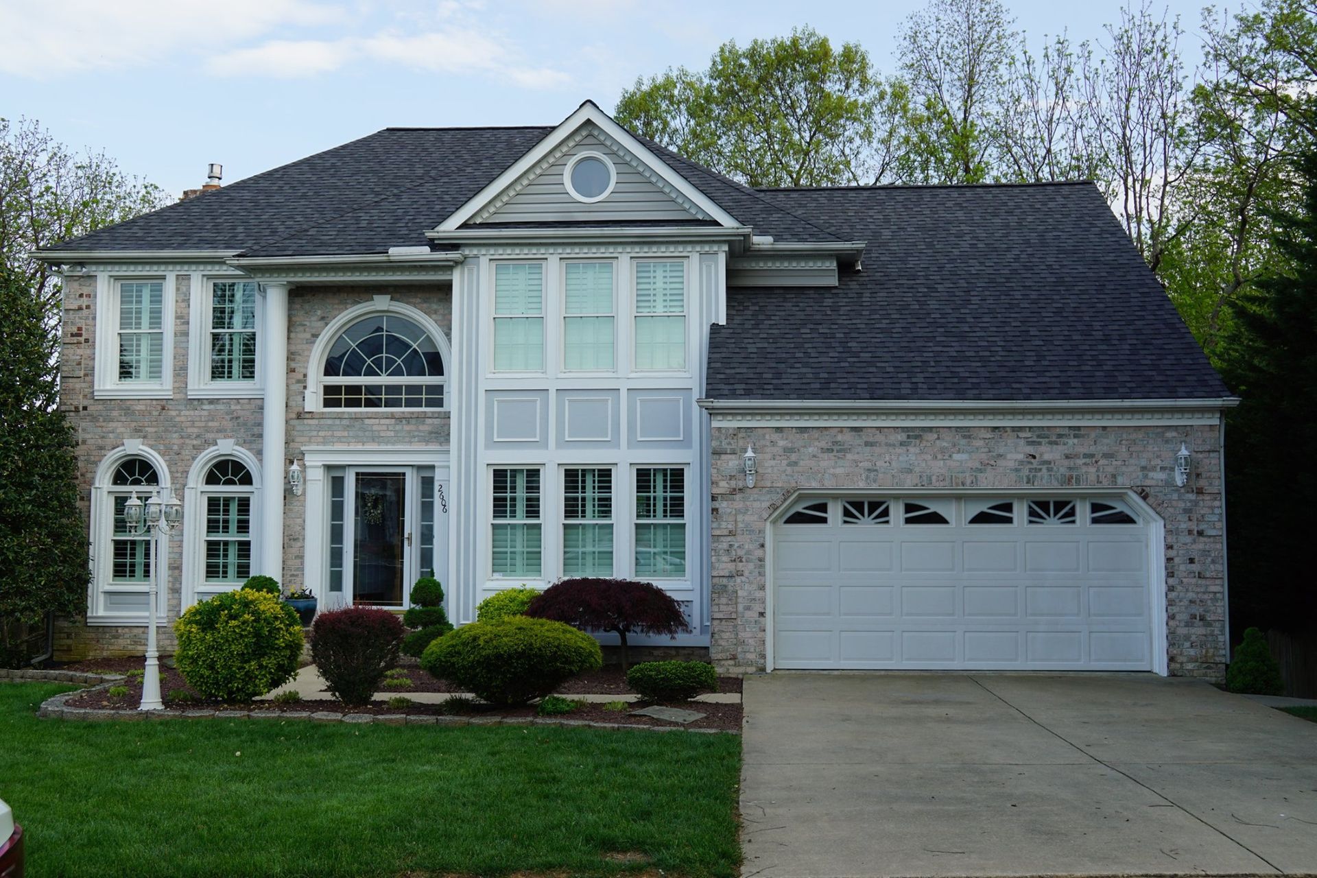 Two-story brick house with a dark gray roof, white trim, and a two-car garage. Landscaping in front.