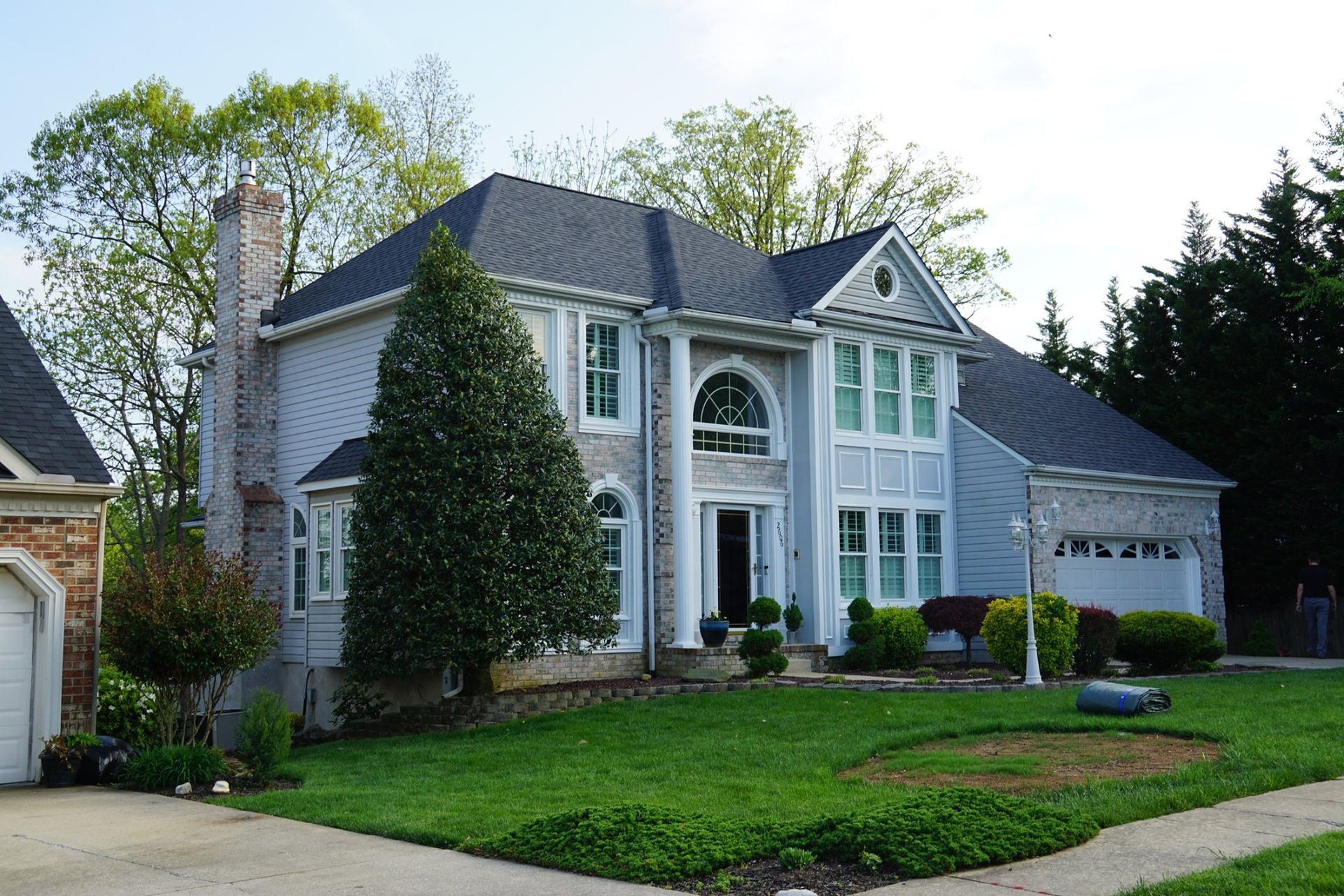 Two-story house with light blue siding, white trim, and a dark gray roof. A well-manicured lawn surrounds the home.
