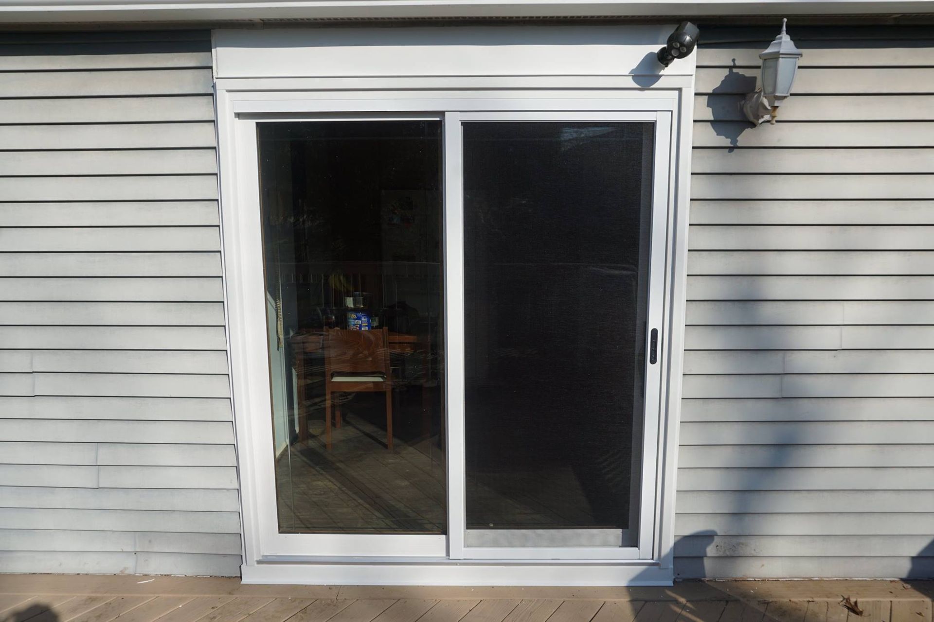 White sliding glass door with a screen, set in a gray-sided wall, and a security camera is visible above the door.