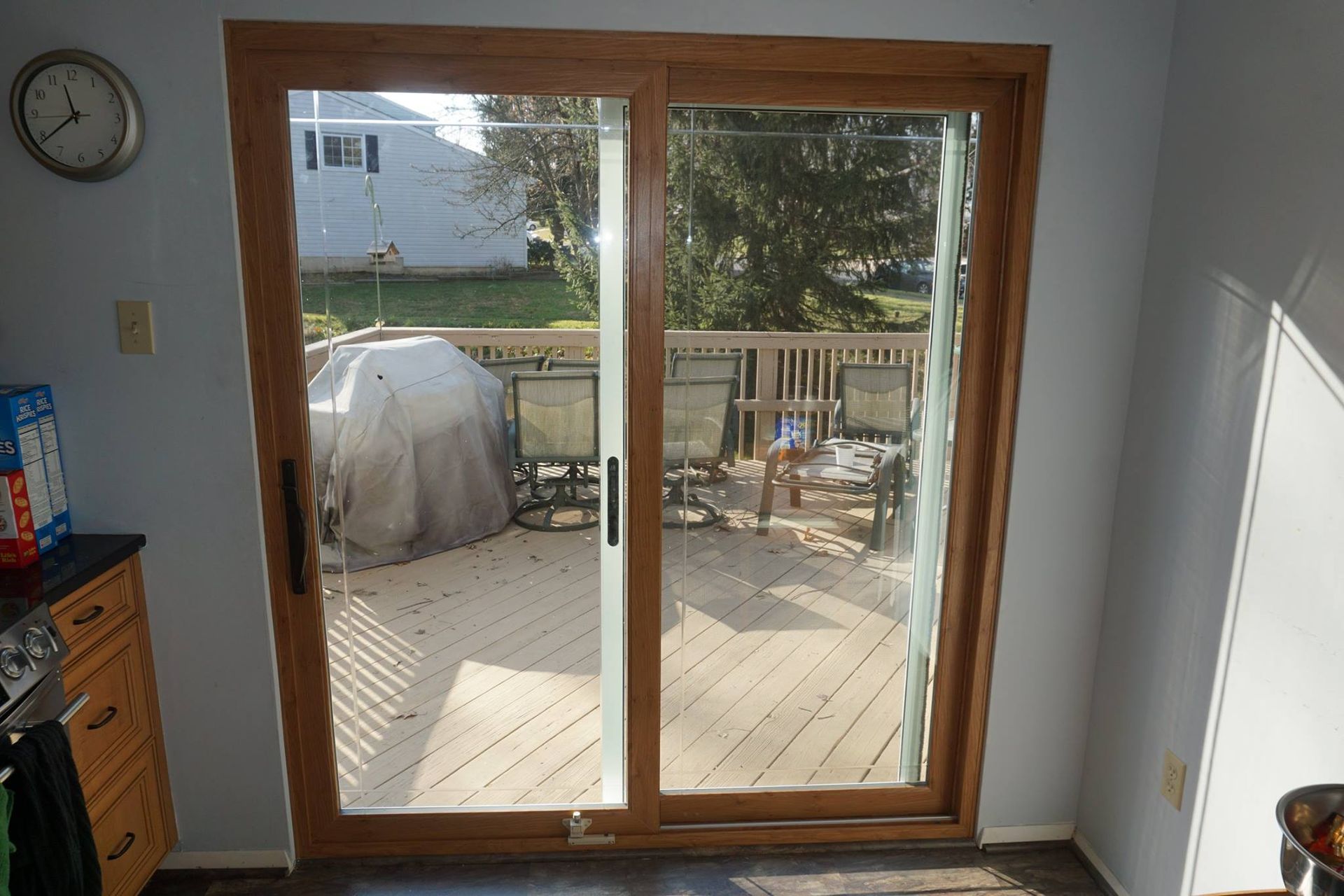 Sliding glass door, wooden frame, leads to a wooden deck with outdoor furniture.