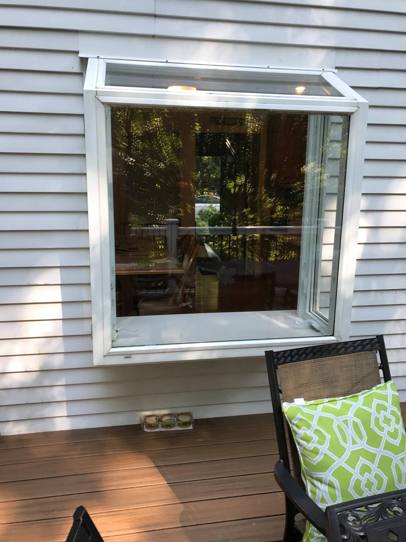White-framed window on a white siding wall. Window opens at the top. Deck and chair in front.