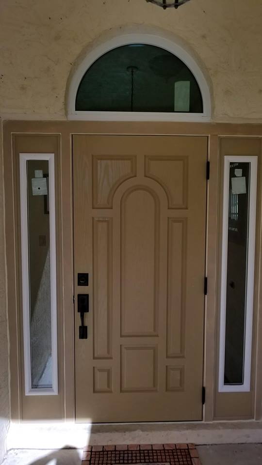 A tan front door with two windows and a white trim.