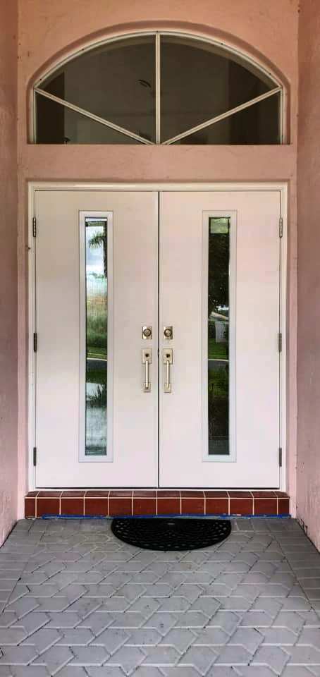 A white double door with a black mat in front of it.