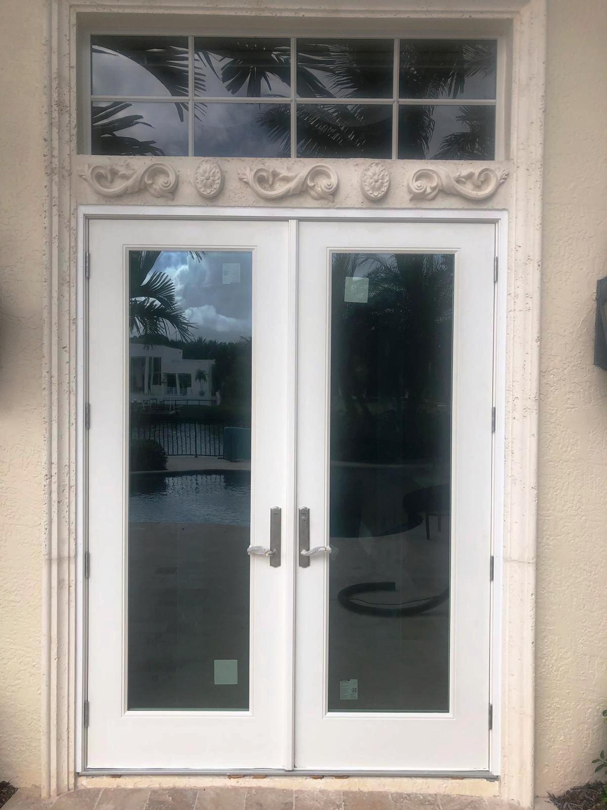 A pair of white french doors with a window above them on a house.