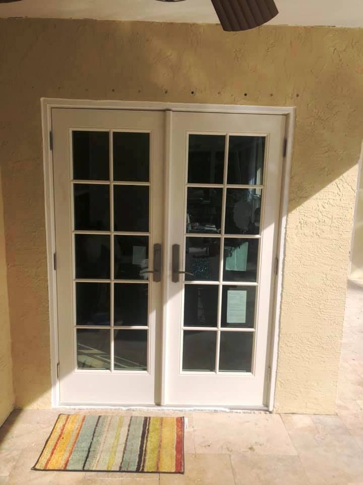 A pair of french doors are open to a patio with a rug on the ground.