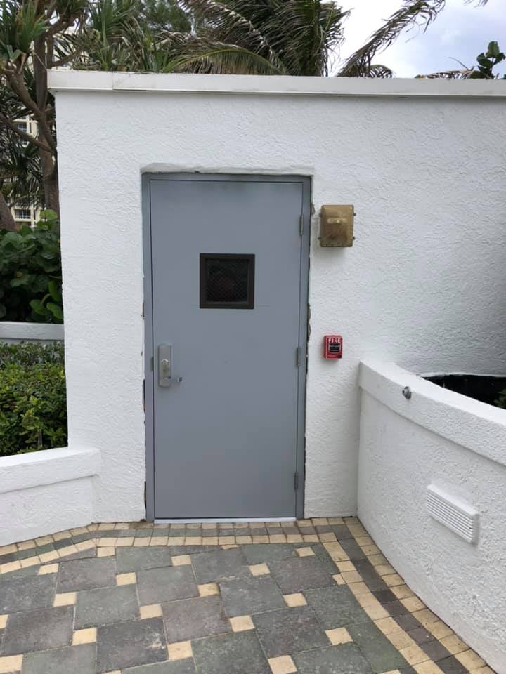 A white wall with a door and a fire alarm on it