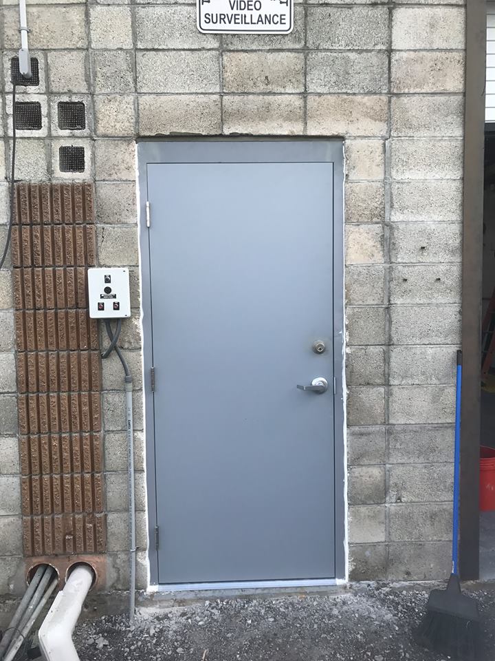 A gray door is on the side of a brick building.