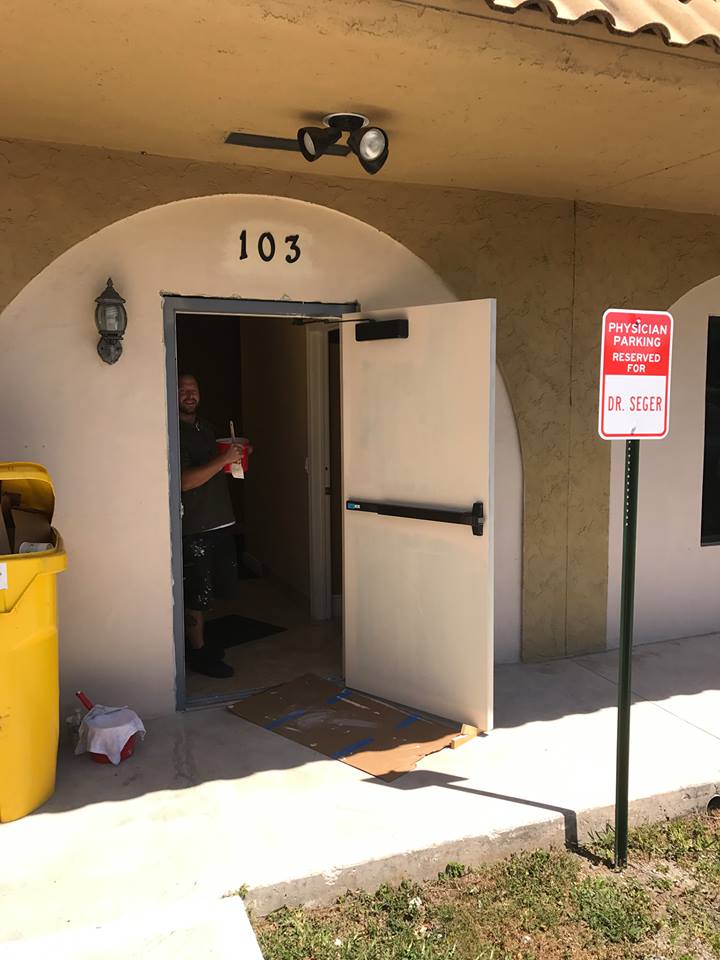 A man is standing in the doorway of a building with the number 103 on it