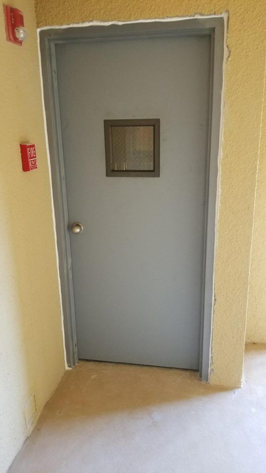 A gray door with a small window in a hallway.