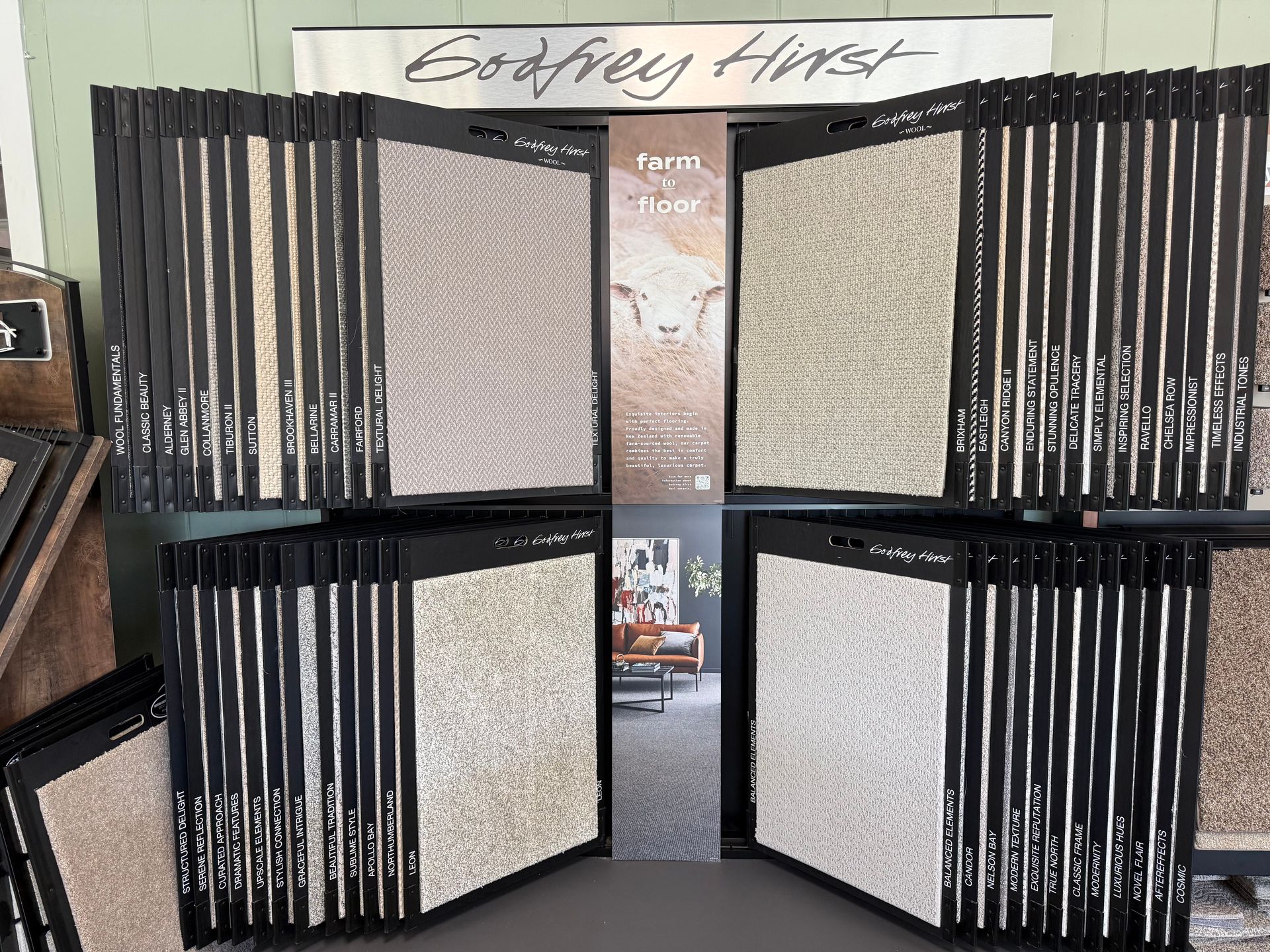 Display of assorted rugs and carpets with black-edged panels in a showroom with a “Godfrey Hirst” sign