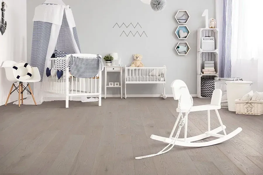 Bright gray nursery with white rocking chair, crib, shelves, and hanging hexagon decor.