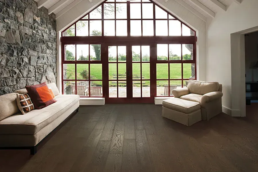 Bright living room with vaulted ceiling, stone wall, beige sofas, and large windows overlooking green fields