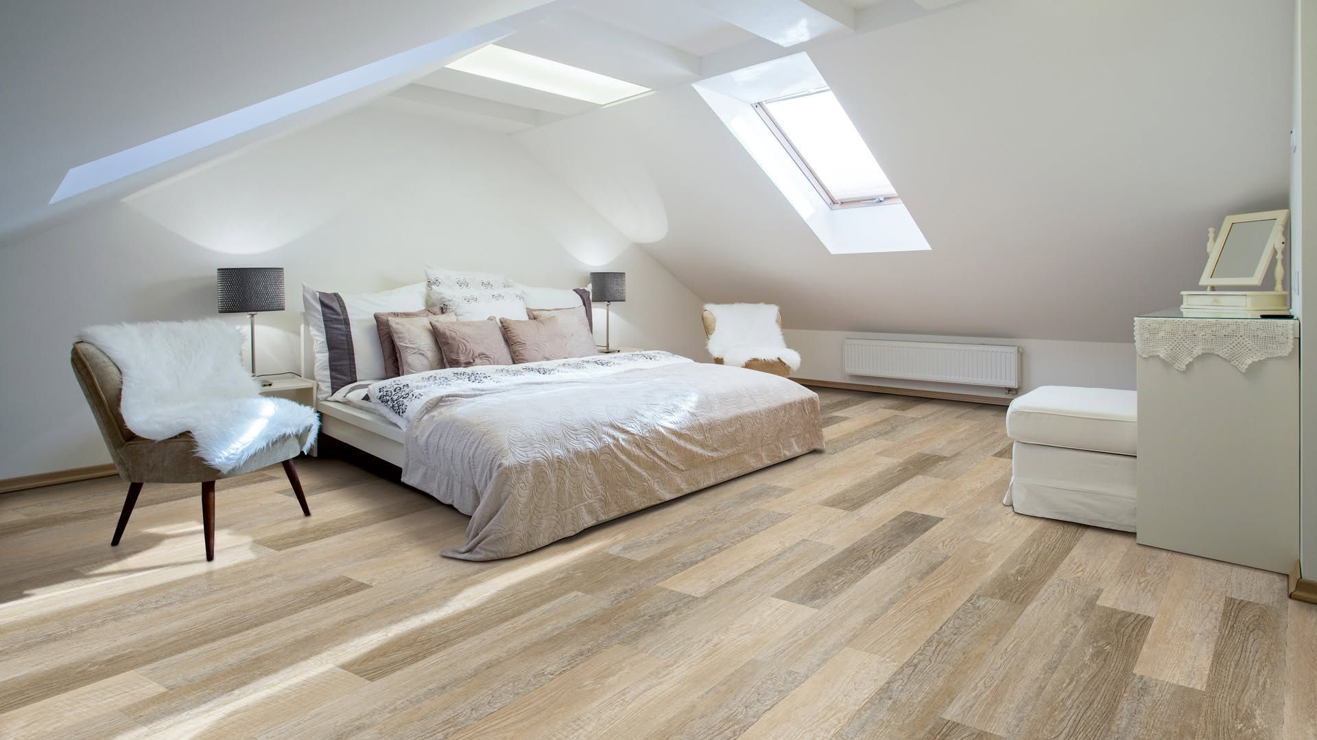 Bright attic bedroom with a large bed, skylight windows, armchair, and white furniture on light wood floors