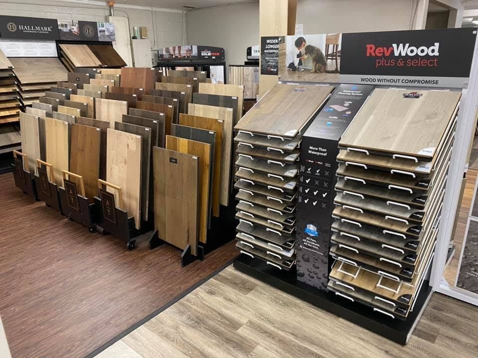 Flooring showroom with wood-look planks and display racks of sample boards, including RevWood flooring displays