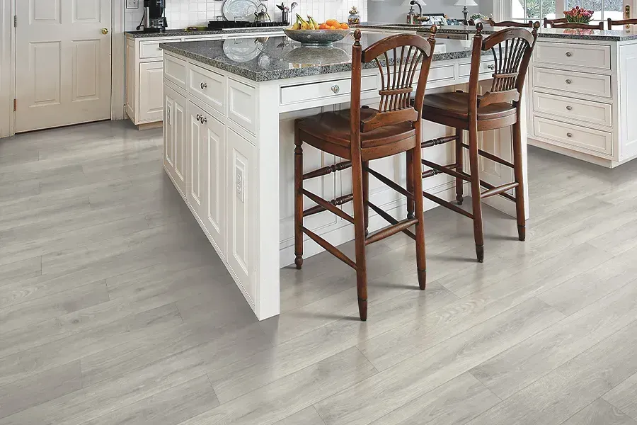 Bright kitchen with white cabinets, gray flooring, and two wooden bar stools by a marble island