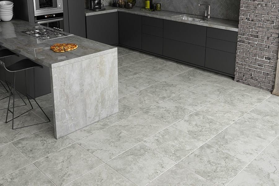 Modern kitchen with gray island, black cabinets, stone floor, and a fruit bowl on the counter