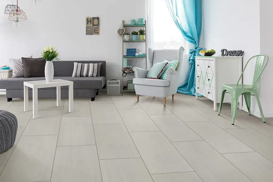 Bright modern living room with gray sofa, white tables, mint chair, blue curtains, and light tile floor