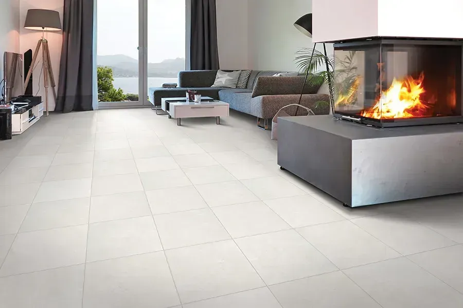 Modern living room with light tile floor, gray sectional sofa, coffee table, and a lit fireplace by large windows