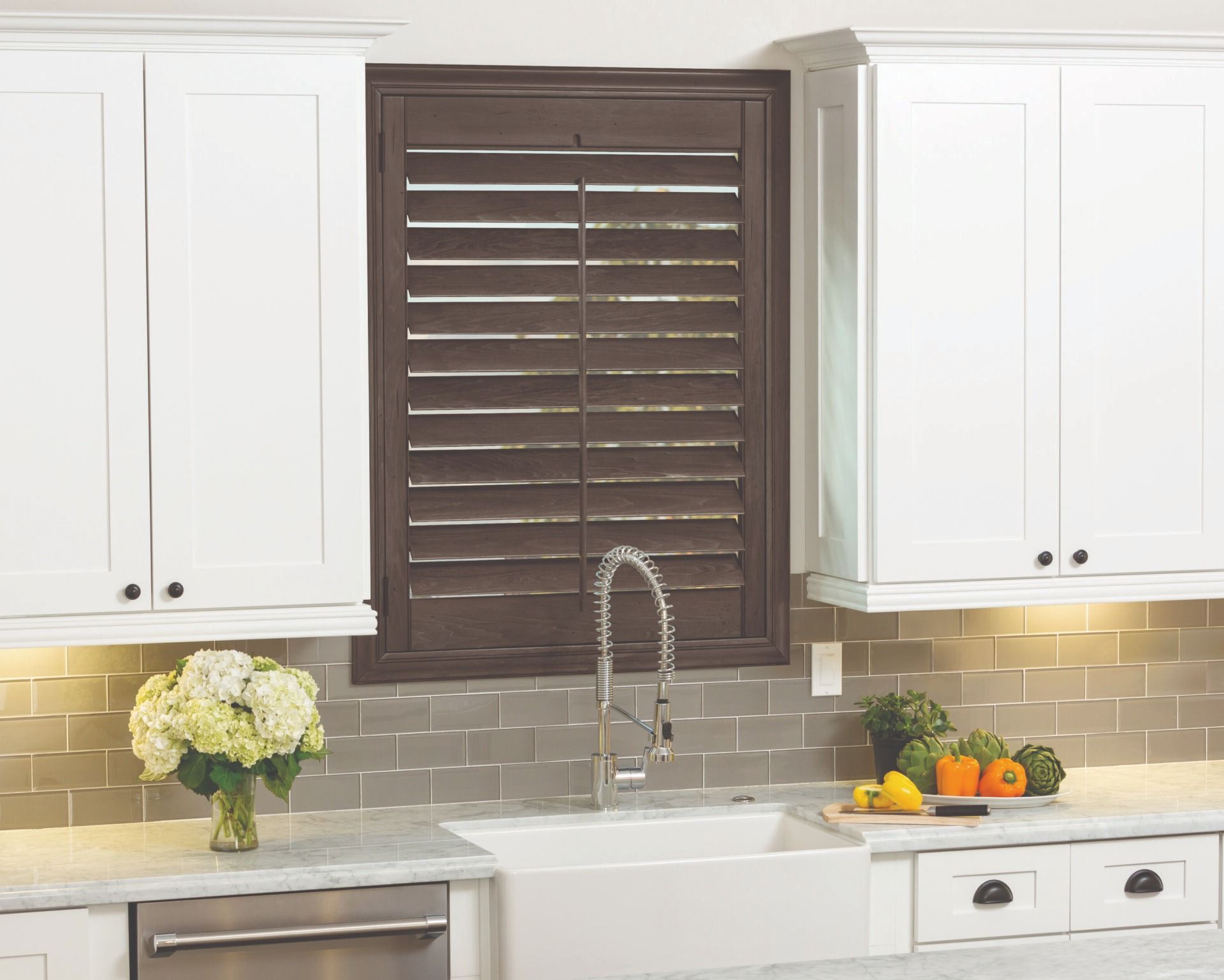 A white kitchen sink area with a dark wood shutter window, gray subway tile backsplash, and white cabinets.