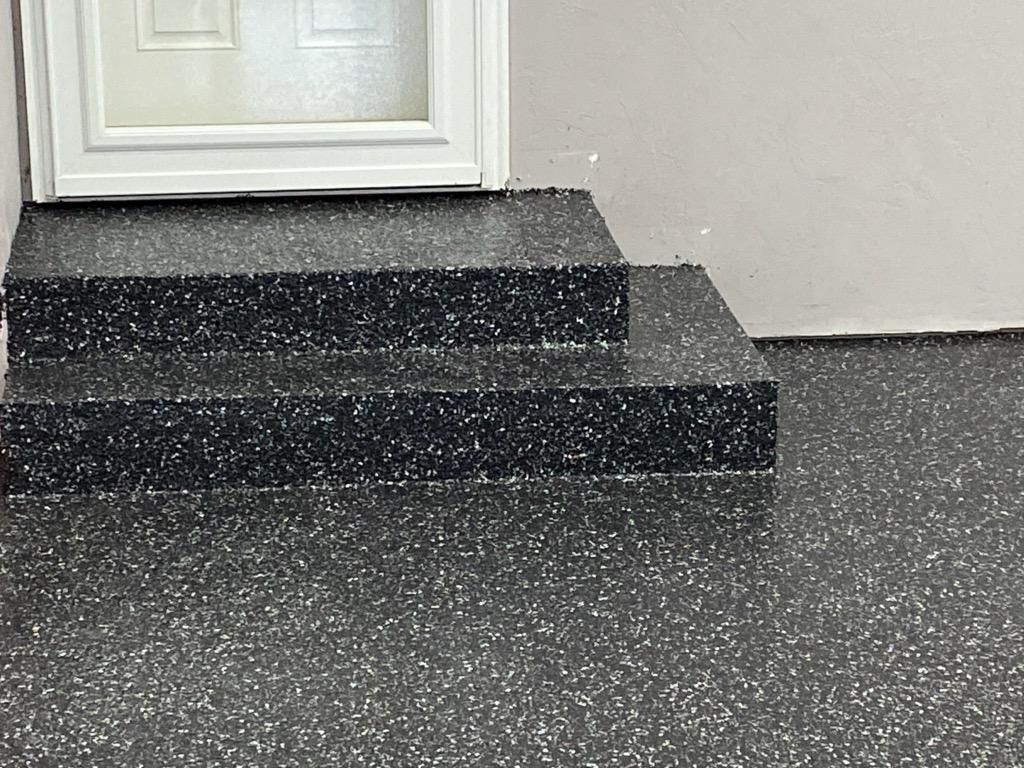 A white door frame sits above two short, steps covered in a dark gray, speckled epoxy or polyaspartic coating.