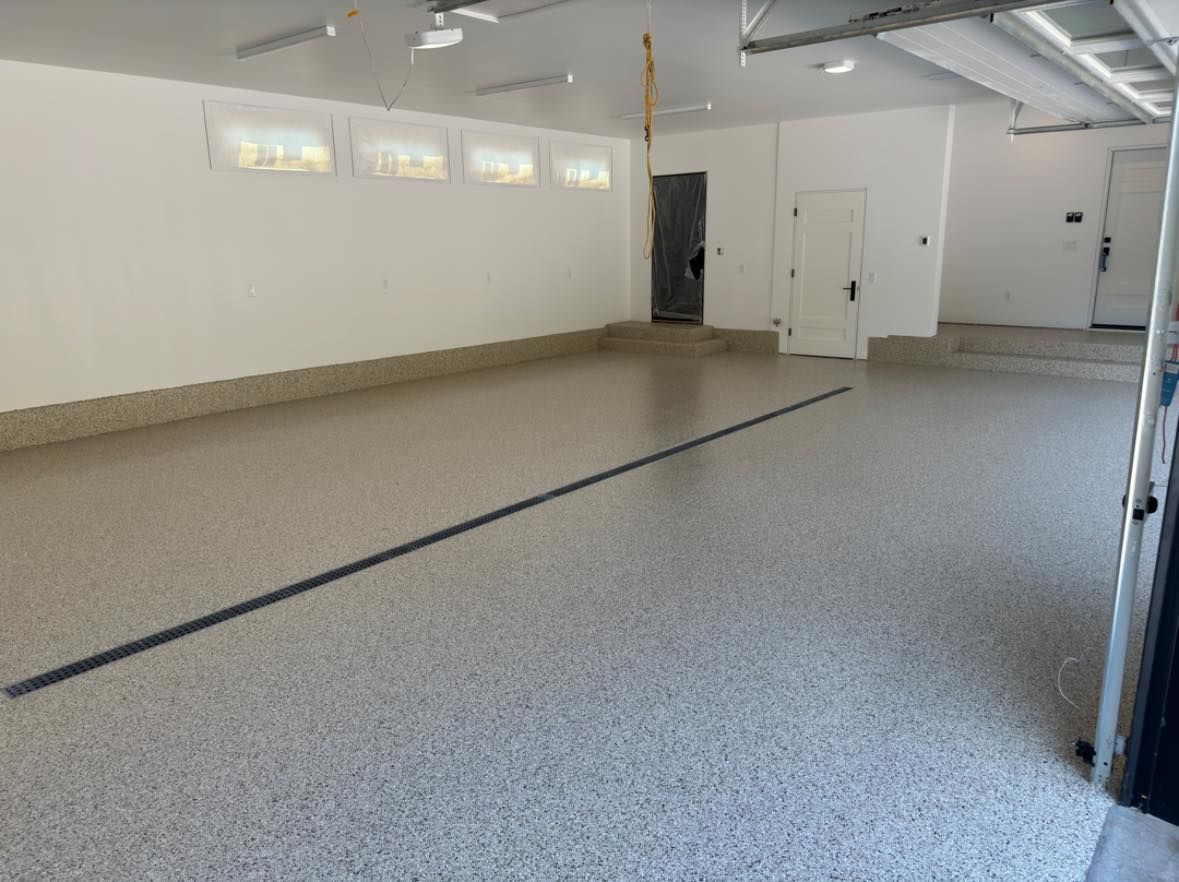 A bright, empty garage with white walls and a light-colored, speckled epoxy floor.