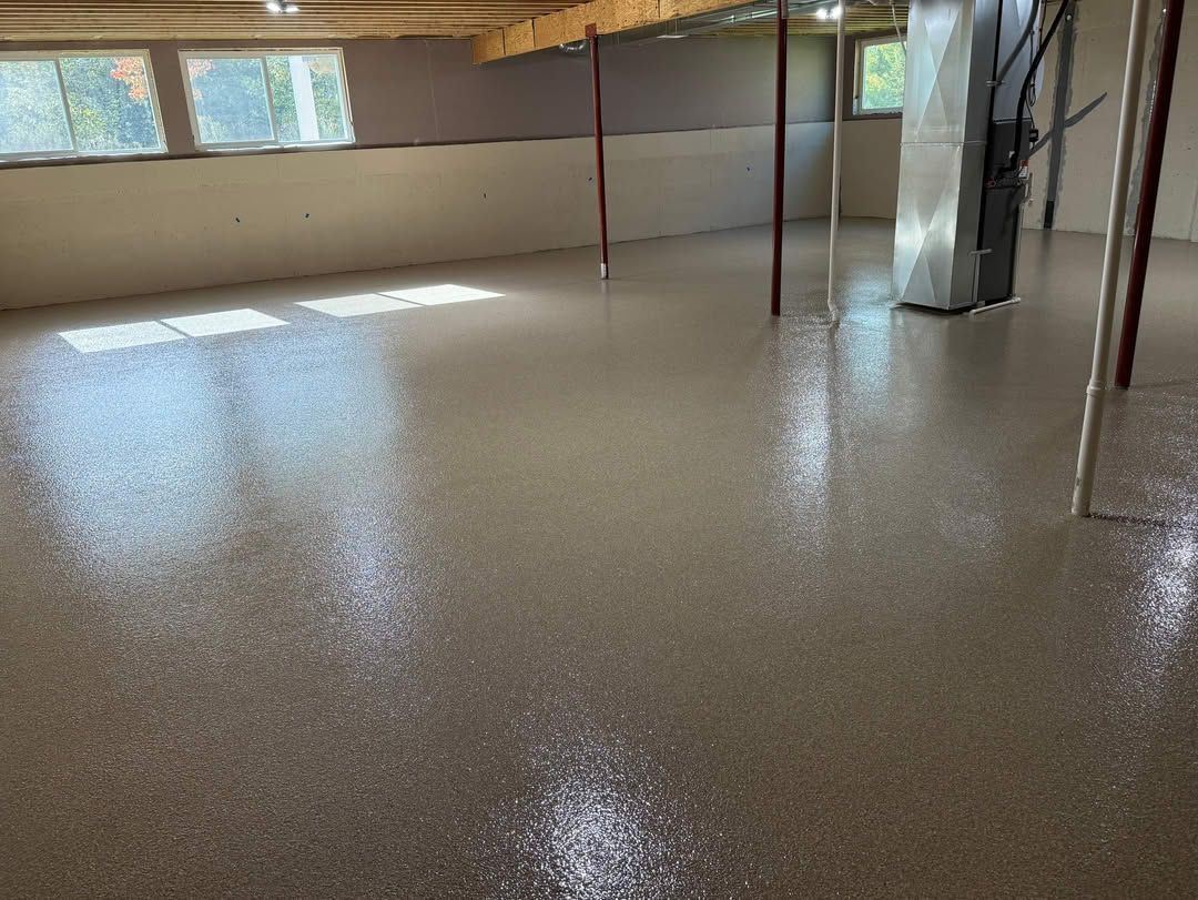 A basement with a freshly applied, high-gloss speckled epoxy floor, support poles, and a central HVAC unit.