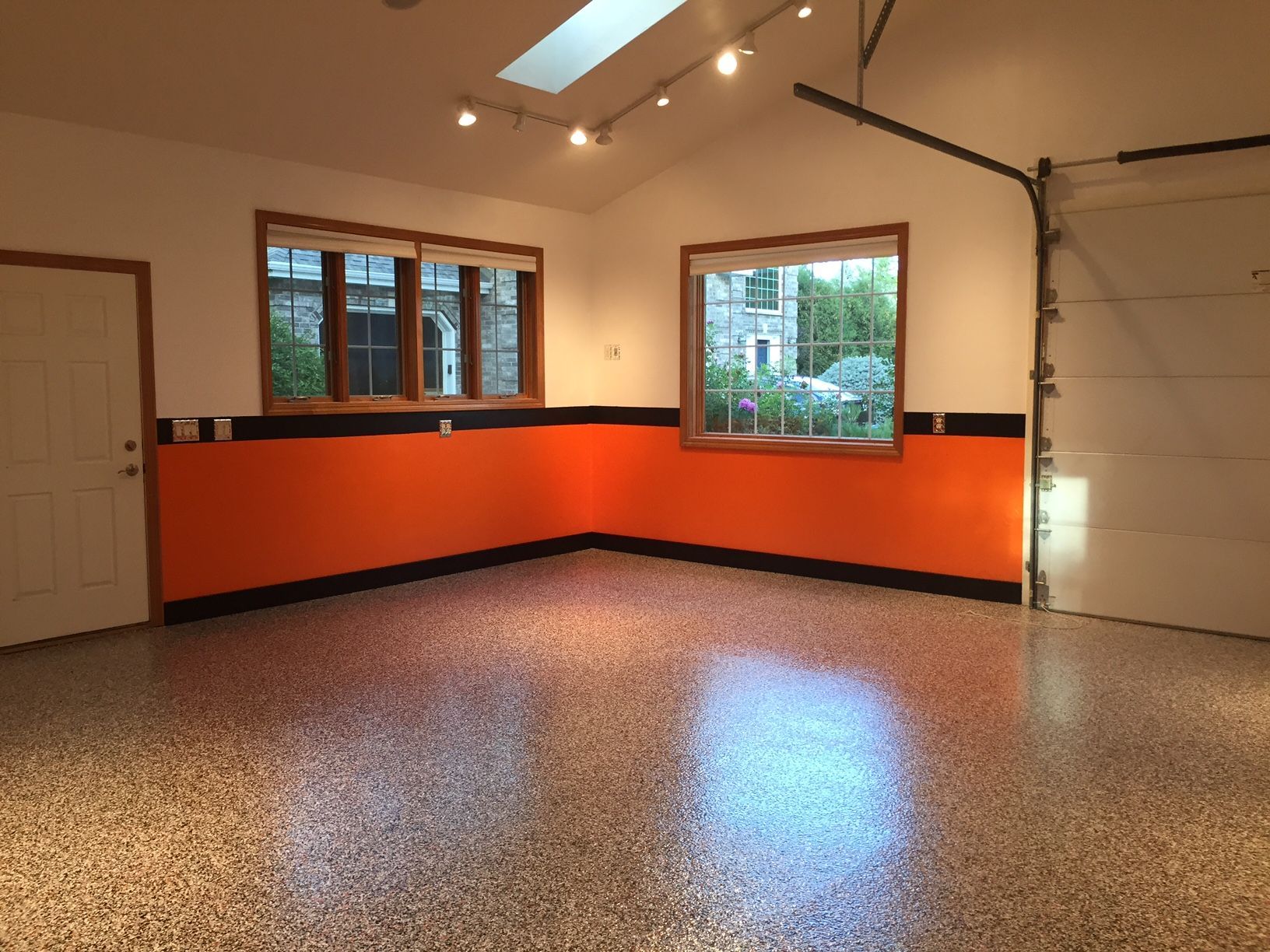 A spacious garage interior featuring bright orange lower walls, tan upper walls, a speckled floor, and track lighting.