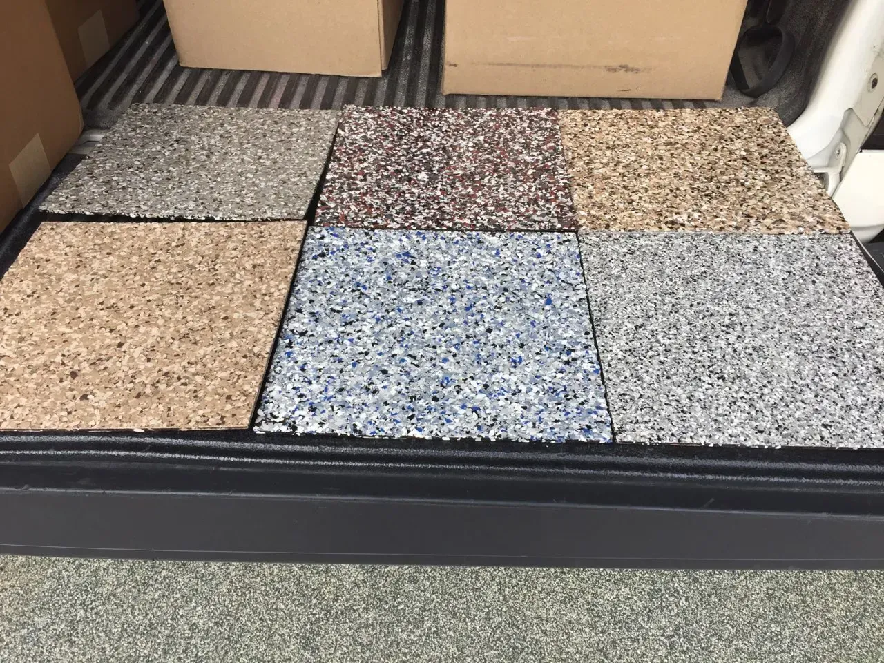 Six square floor tile samples with speckled, textured finishes in shades of gray, brown, tan, and blue.