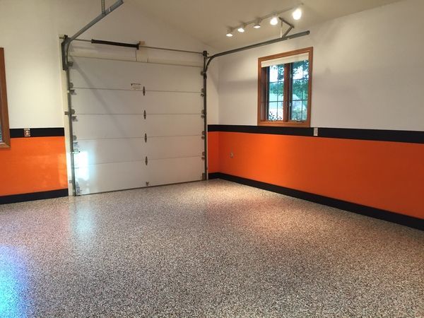 A bright garage with speckled epoxy flooring, orange lower walls with black trim, a garage door, and a small window.