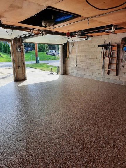 A garage interior featuring a freshly finished brown, tan, and black speckled epoxy floor, with an open door to the outside.
