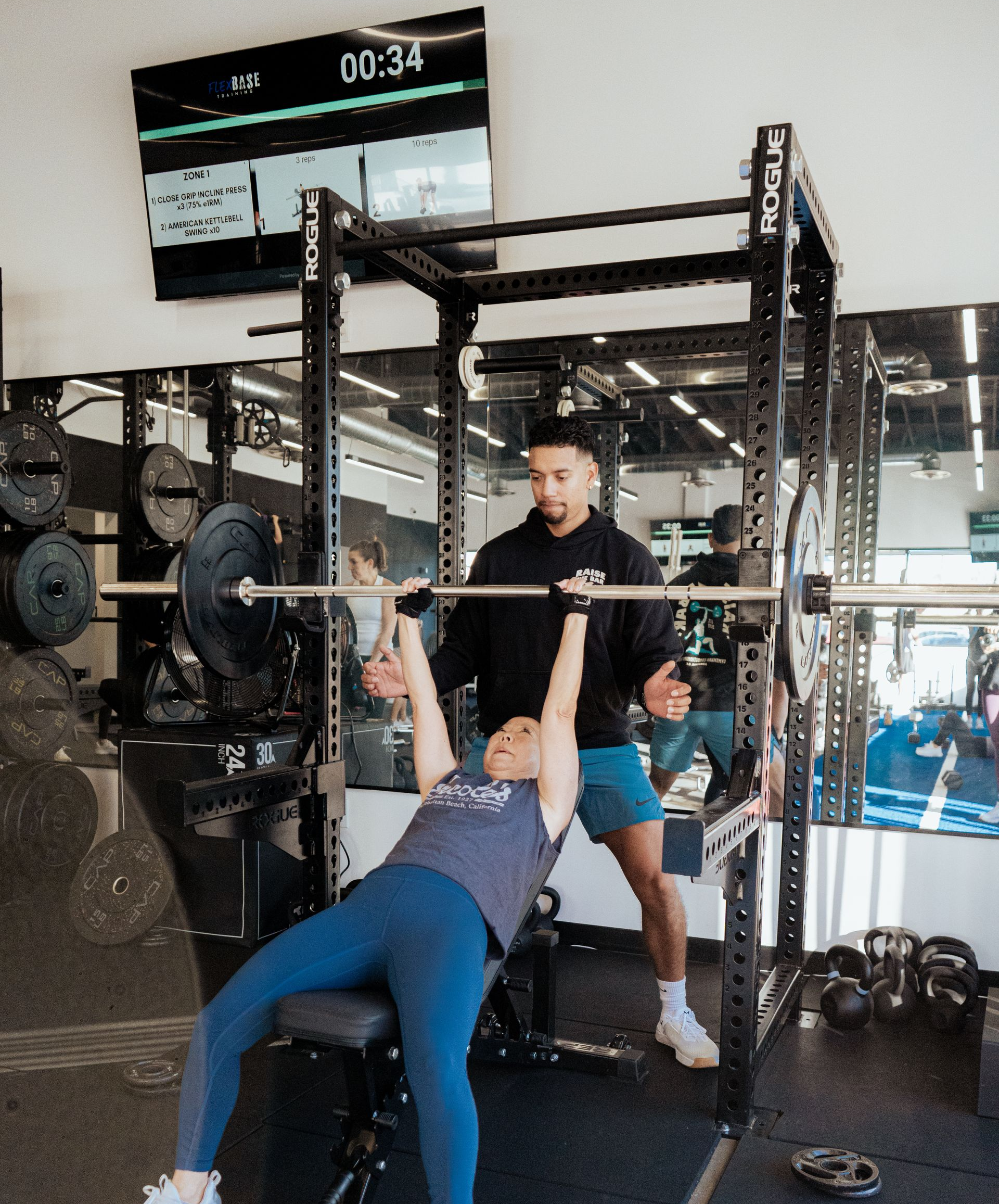 Woman bench presses with spotter in gym, working out with weights.